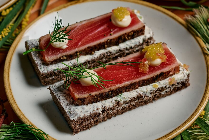 An open-faced cured fish canapé on dark rye bread on a white plate.