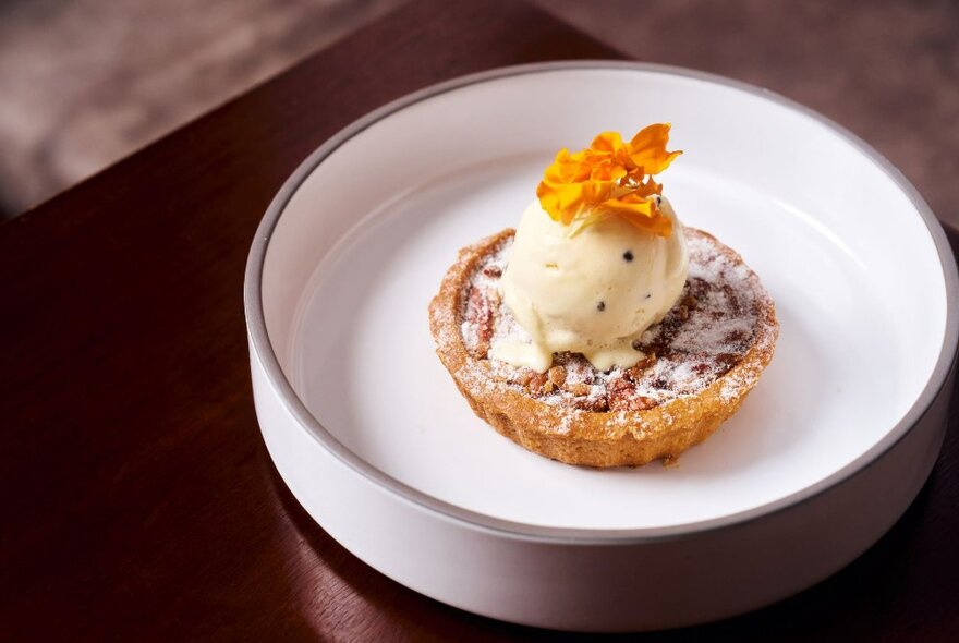 A single pastry dessert on a white plate, topped with a scoop of ice-cream and a floral garnish.