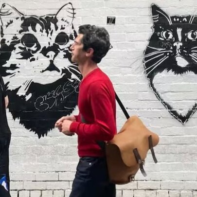 People walking past stencil artwork of cats on a white wall in a Melbourne laneway.