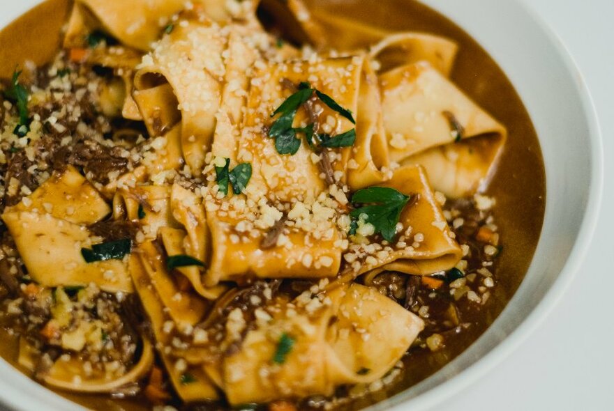 A brown bowl of large ribbon pizza dotted with cheese and parsley.