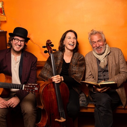 Two musicians and a man with a book in an orange room.
