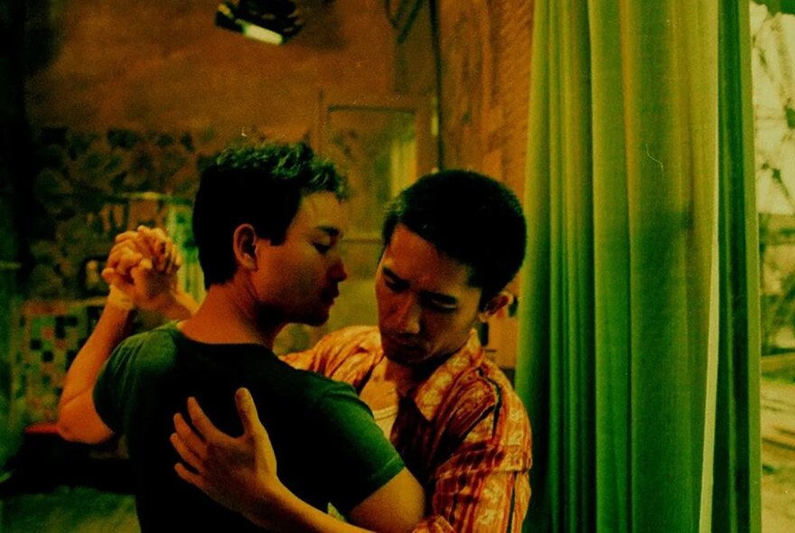 Film still of two men facing each other and dancing a slow dance, seen from the torso up.