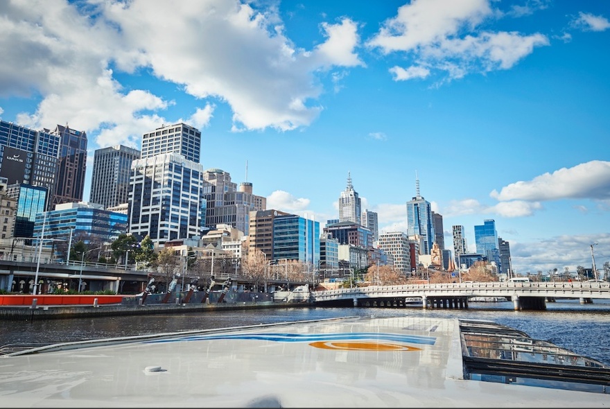 Cruise boat on Yarra River with buildings and bridge.