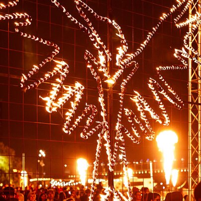 An illuminated fire sculpture at the entrance to the Firelight Festival at Docklands, with a crowds of people wandering around underneath.