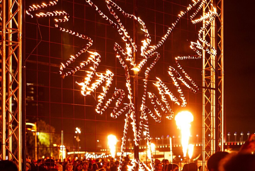 An illuminated fire sculpture at the entrance to the Firelight Festival at Docklands, with a crowds of people wandering around underneath.