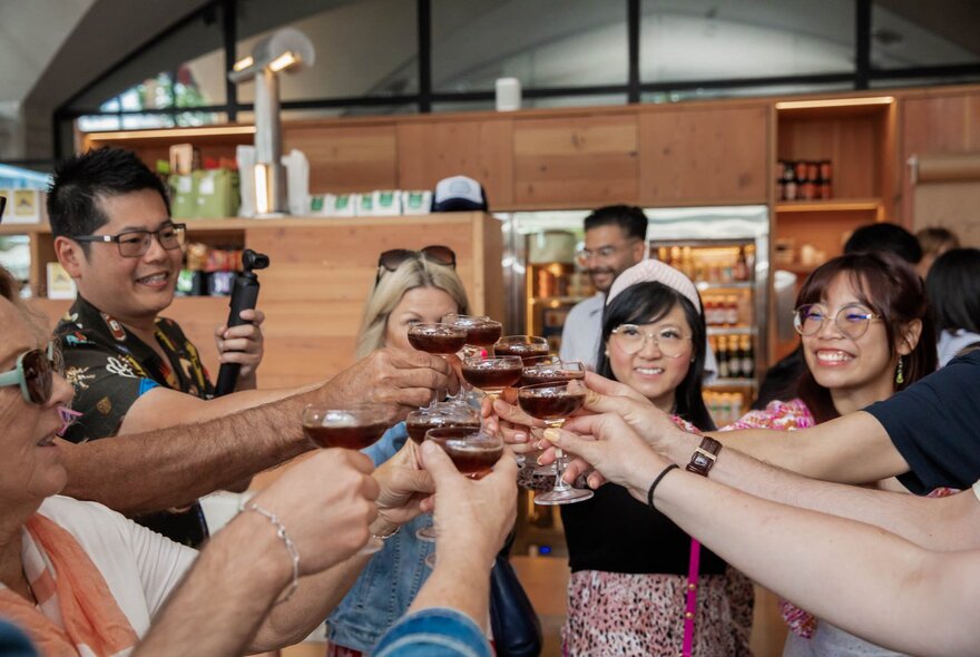 A group of smiling people on a food tour at Queen Victoria Market, all raising a beverage in a glass in a toast.