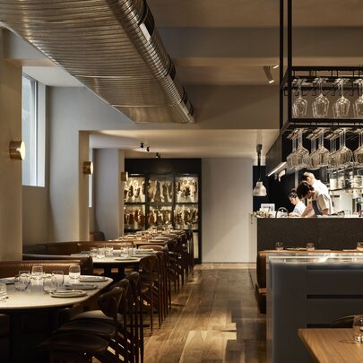 Interior of Nomad restaurant showing tables set and ready for dining patrons, with the open kitchen area visible in the background.