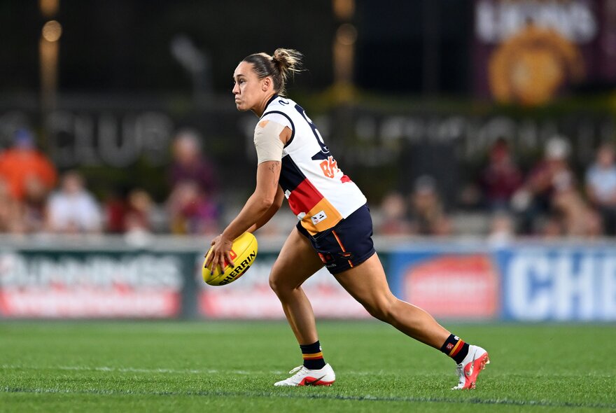 An Adelaide Crows AFLW player running on the field with the football in her hands about to kick it.