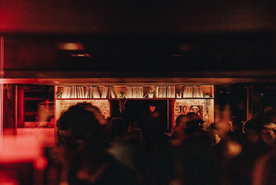 Dimly lit underground bar, with musicians performing on a small stage at the rear of the venue, and people blurred in the foreground.