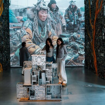 Two young adults observing a sculpture in a gallery space with digital and scupltural displays.