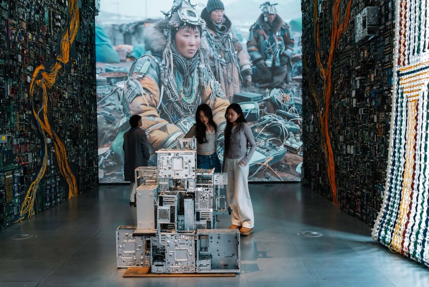 Two young adults observing a sculpture in a gallery space with digital and scupltural displays.