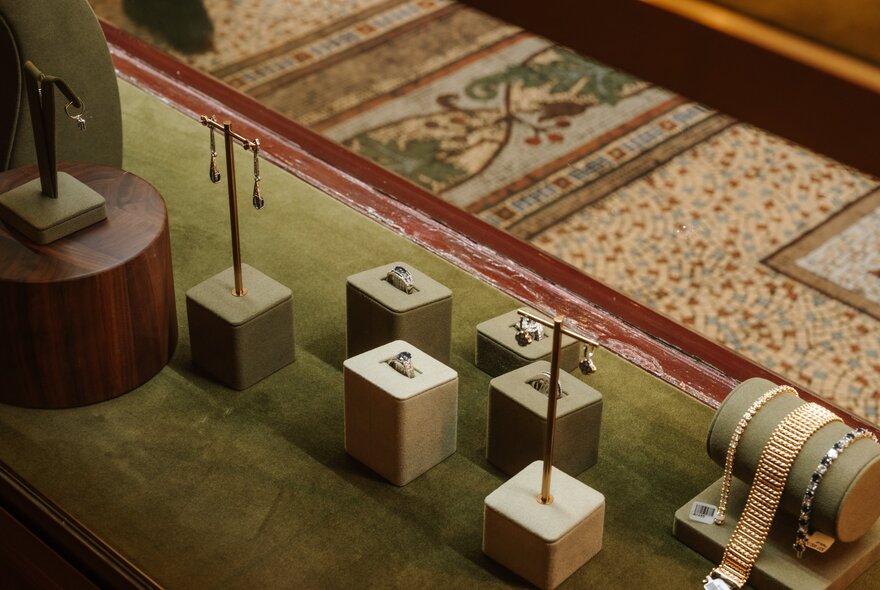 Small jewellery pieces displayed in a case lined with olive green velvet.