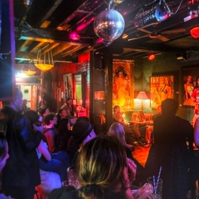 Crowded, dimly lit bar with mirror ball, artworks on the walls and eclectic decor.