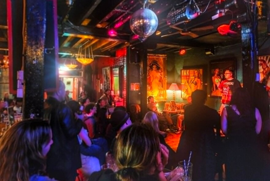 Crowded, dimly lit bar with mirror ball, artworks on the walls and eclectic decor.