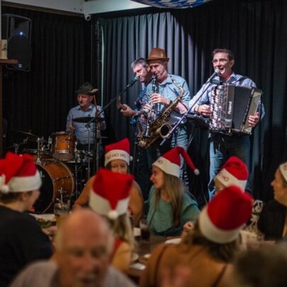 A German band performing on stage to a crowd wearing santa hats.