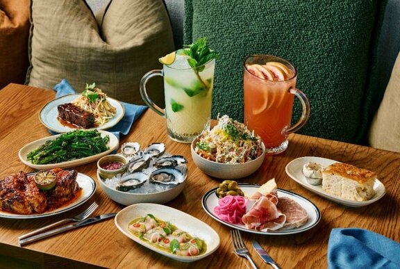 Restaurant table with eight dishes of food and jugs of cocktails.