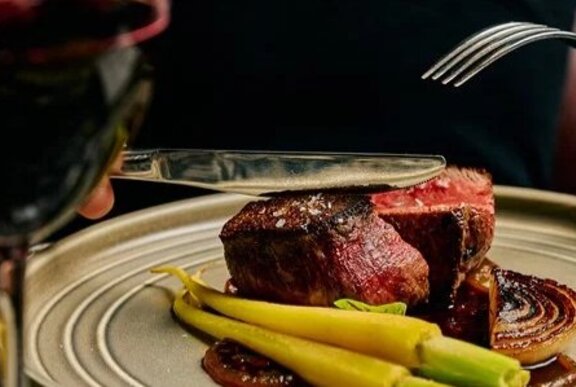 Plate of meat and vegetables with a glass of red wine.