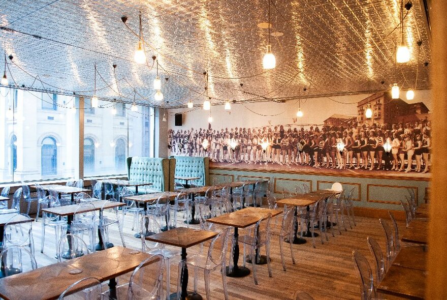 Large and airy restaurant interior with rows of tables and chairs, and lights reflected in the pressed-tin ceiling.