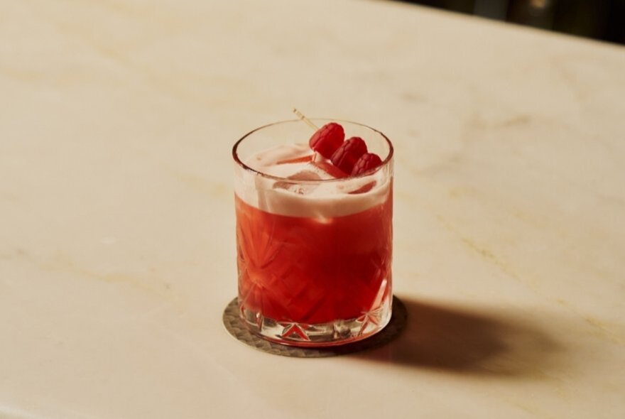 Red cocktail with garnish on a marble table.