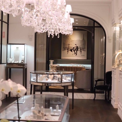 White-walled shop interior, with large painting at rear, display cases in middle, large chandelier from ceiling.