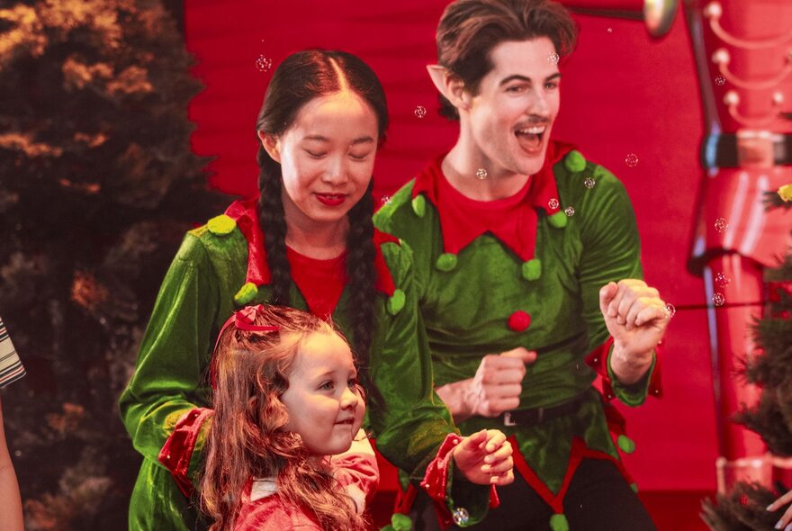 Two performers dressed as Christmas elves and interacting with a young child during a live family show.
