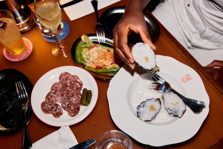 A table with snack plates and cocktails and someone taking an oyster.