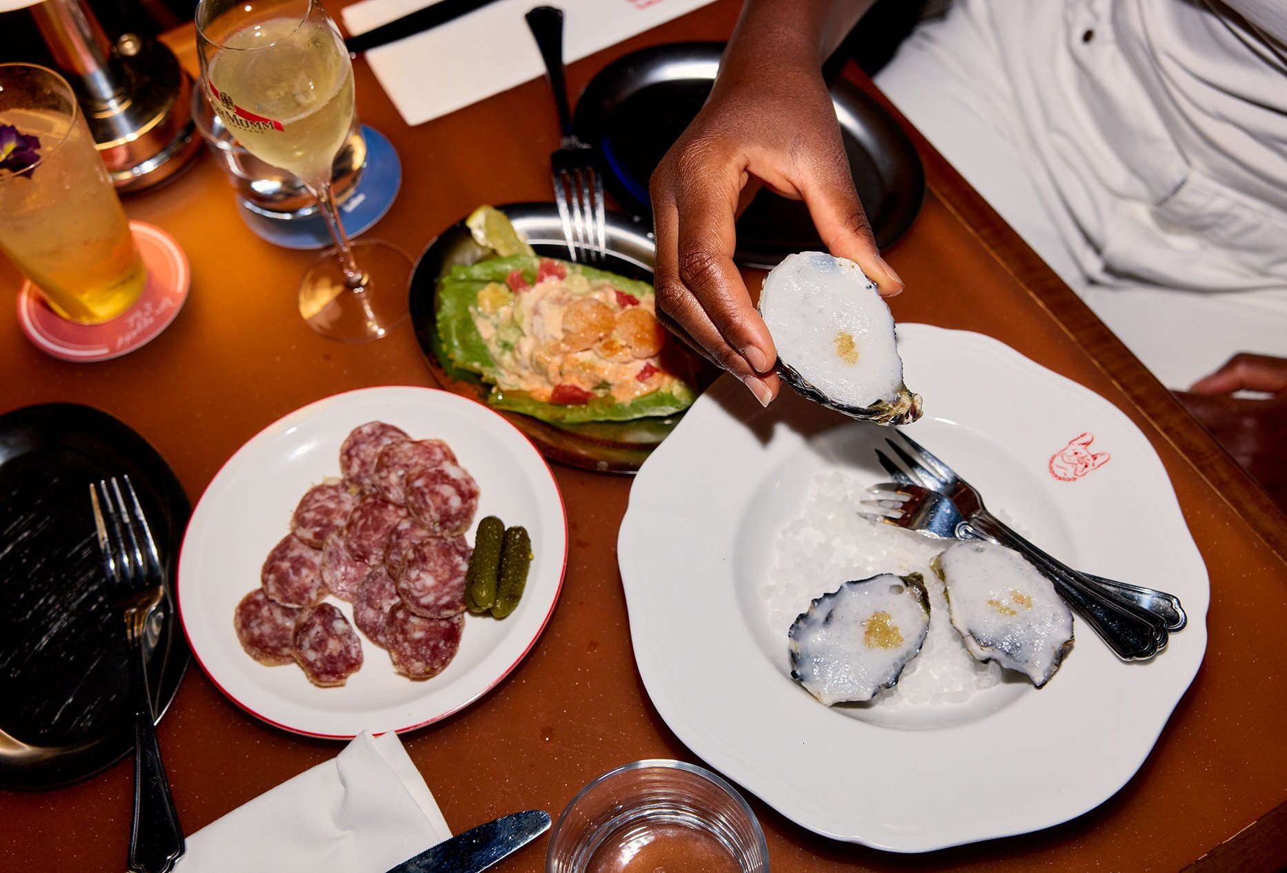 A table with snack plates and cocktails and someone taking an oyster.
