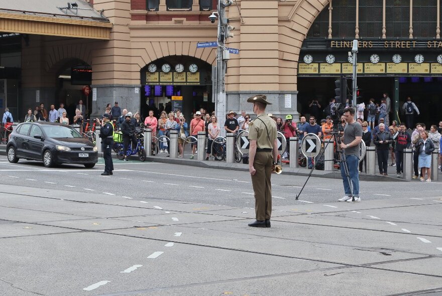 A man in Australian Army uniform standing in the middle of the intersection outside Flinders Street Station.