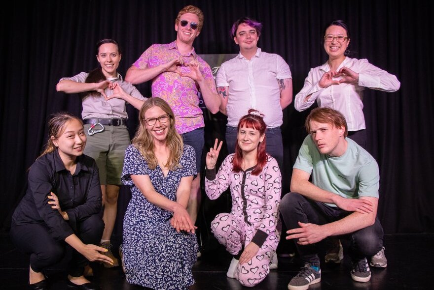 Group of eight people against black stage curtain laughing and posing.