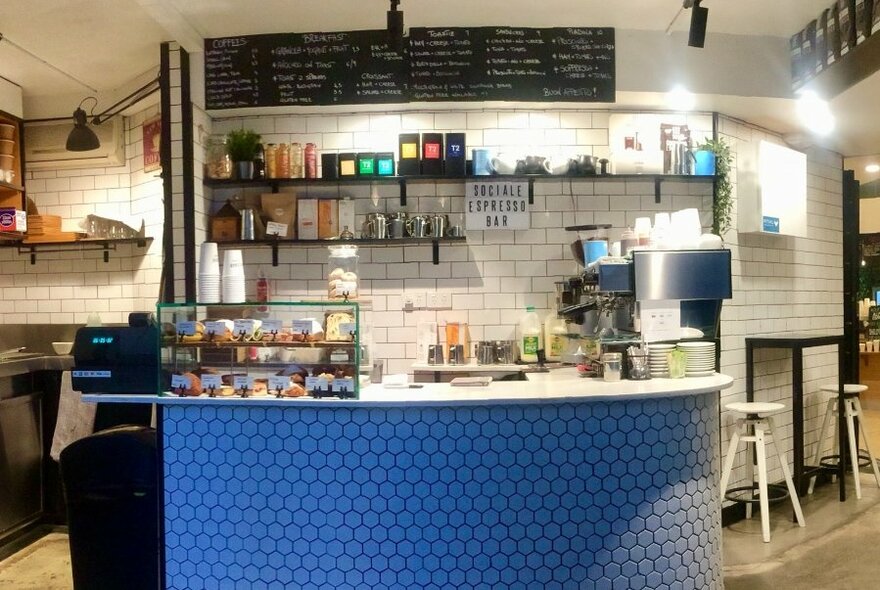 Interior of Sociale Espresso Bar: blue tiled counter beneath black shelves and menu boards.