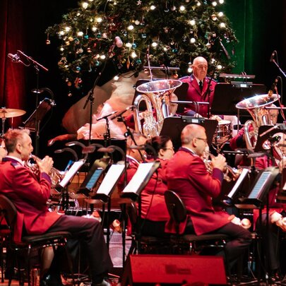 An orchestra dressed in red suits playing on a stage that is decorated in festive and seasonal Christmas decorations.