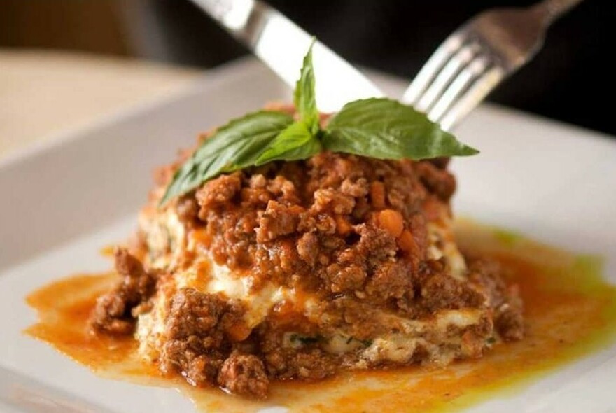 Knife and fork cutting into a meat dish garnished with basil.