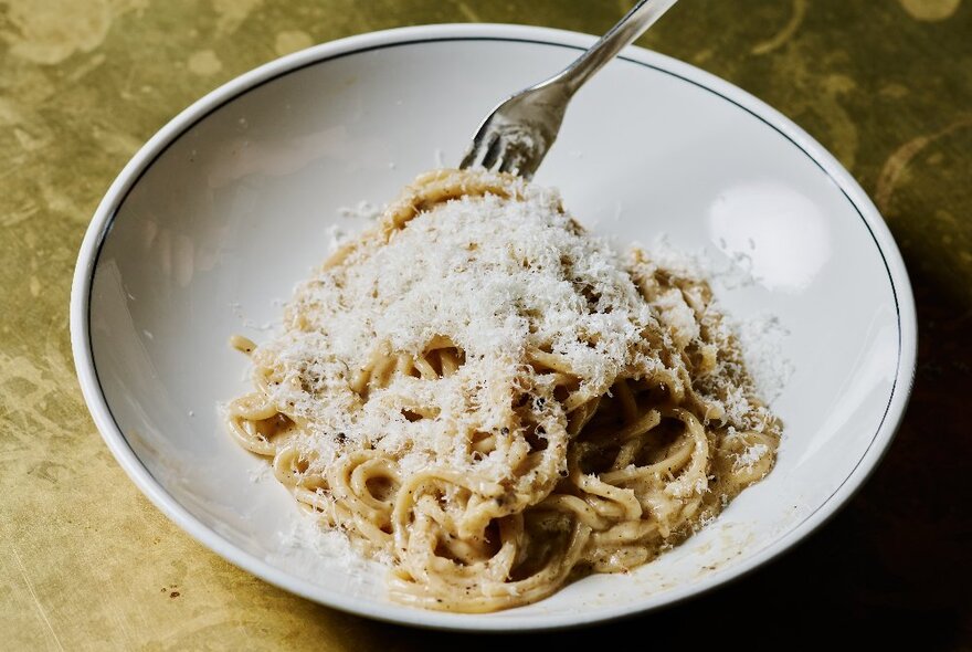 A bowl of cacio e pepe pasta with lots of grated parmesan cheese on top.