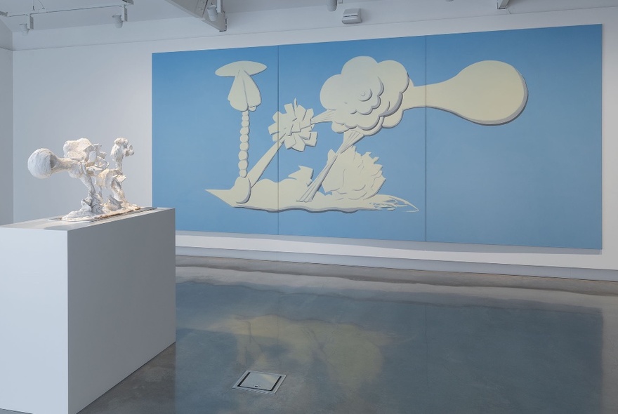 Large blue and white Wedgwood-inspired artwork panel on a white gallery wall, a white bench with white sculpture in the foreground.