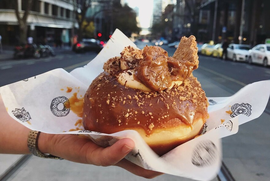 Person displaying a very large, chocolate-filled,  doughnut in the street.