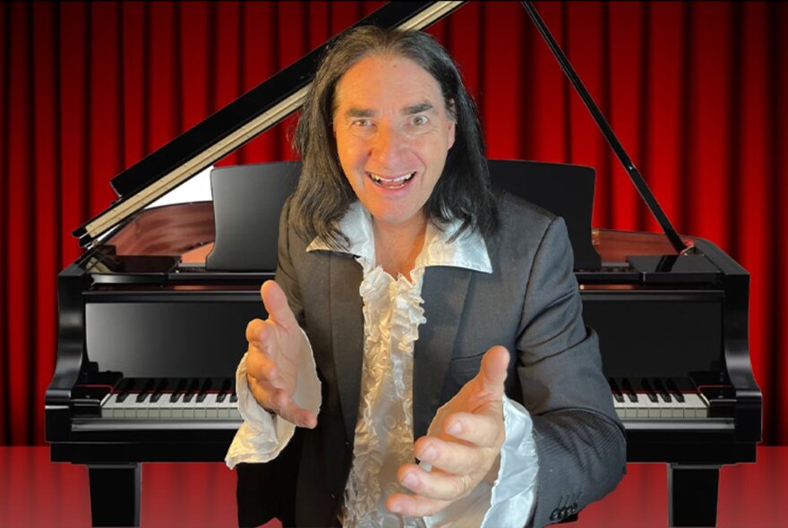 A performer dressed as Meat Loaf in a suit and ruffled shirt, standing in front of a black grand piano and red stage curtain.