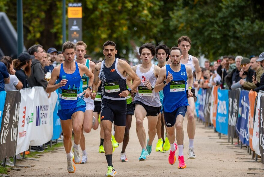 A team of runners wearing athletic shorts and dayglo runners passing lines of spectators.