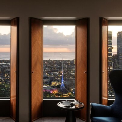 View out of a window of the Melbourne skyline from a room at the Sofitel on Collins, with a large armchair and small table positioned in front of the window.