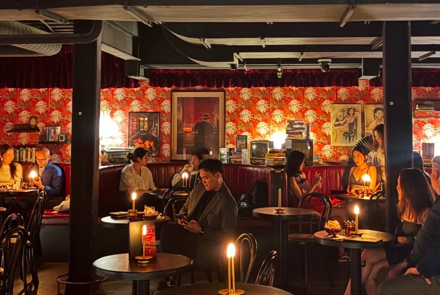 A cosy bar with booths and round tables in front of a patterned wall.