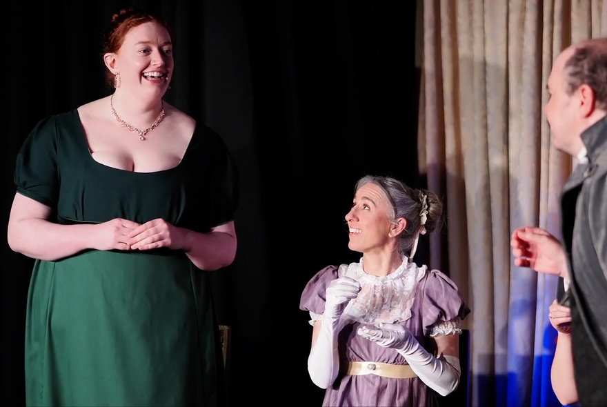Three performers dressed in Regency outfits holding imaginary cups of tea.
