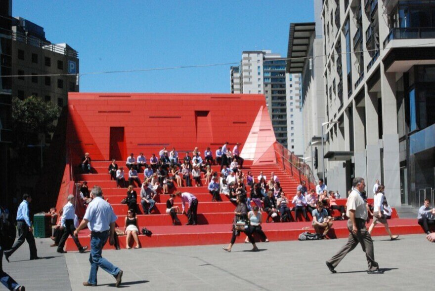 People sitting on a large red stair case in the city.