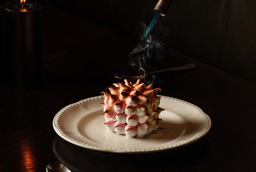 Pine-cone-shaped bombe Alaska on a white plate, with a little steam.