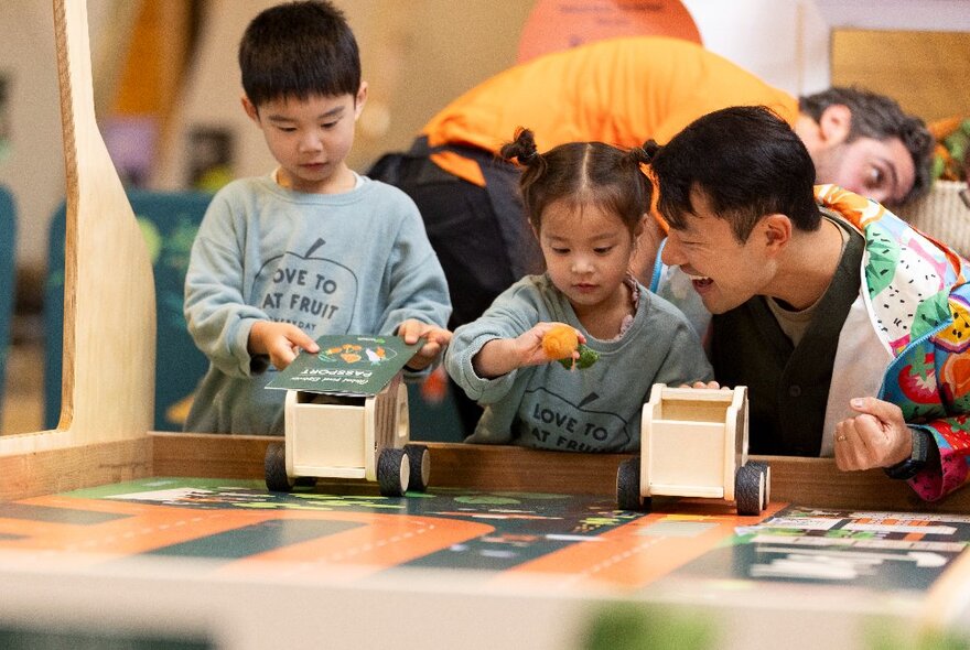 Children and their father exploring a tabletop activity with wooden cars at a museum.