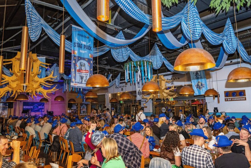 A large room with many seated diners, blue bunting and streamers handing from the roof. 