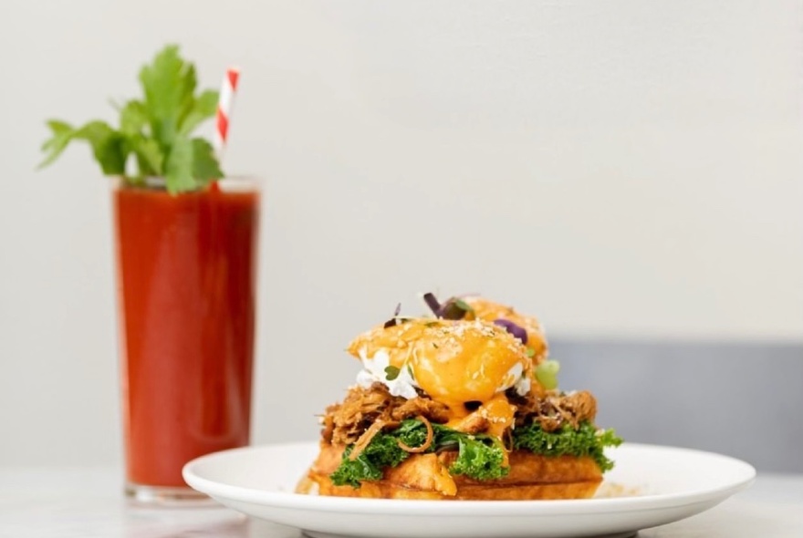 A cooked egg breakfast piled high on a plate, with a glass of tomato juice in the background. 