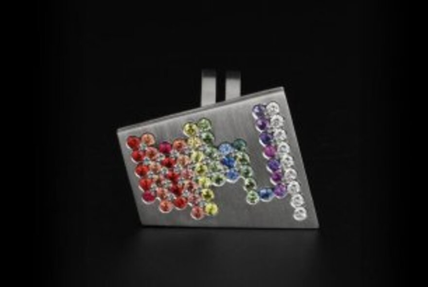 A silver ring embedded with colourful stones against a black background.