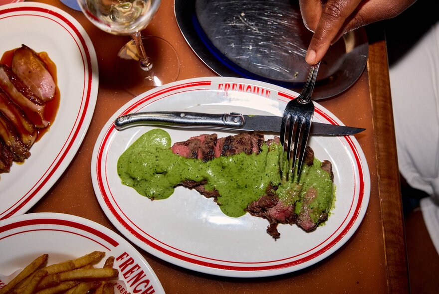 A sliced steak covered in green herb sauce in a restaurant.