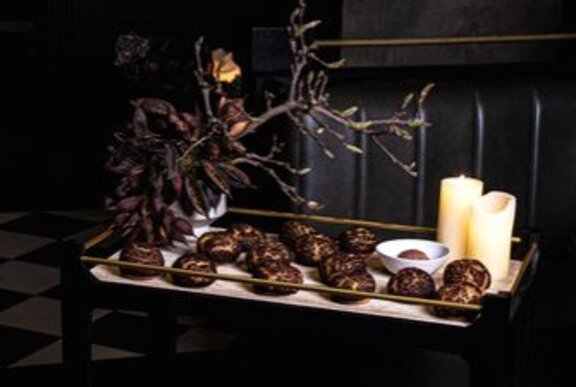 Chocolate choux buns on a trolley in a room with dark tones and a decorative branch. 