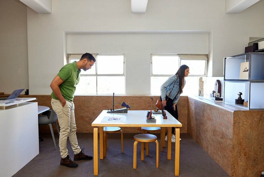 Two people looking at artworks on display in a small white room.