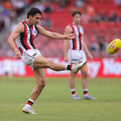 A St Kilda AFL football player with his leg in mid-air having just kicked the yellow football during a match.